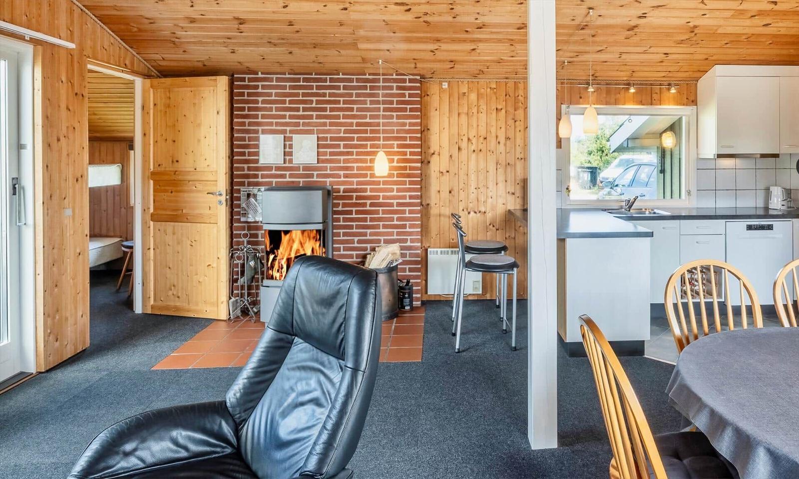 Wohnbereich mit Kamin, Essbereich und Küche. Holzwände und Bodenfliesen.