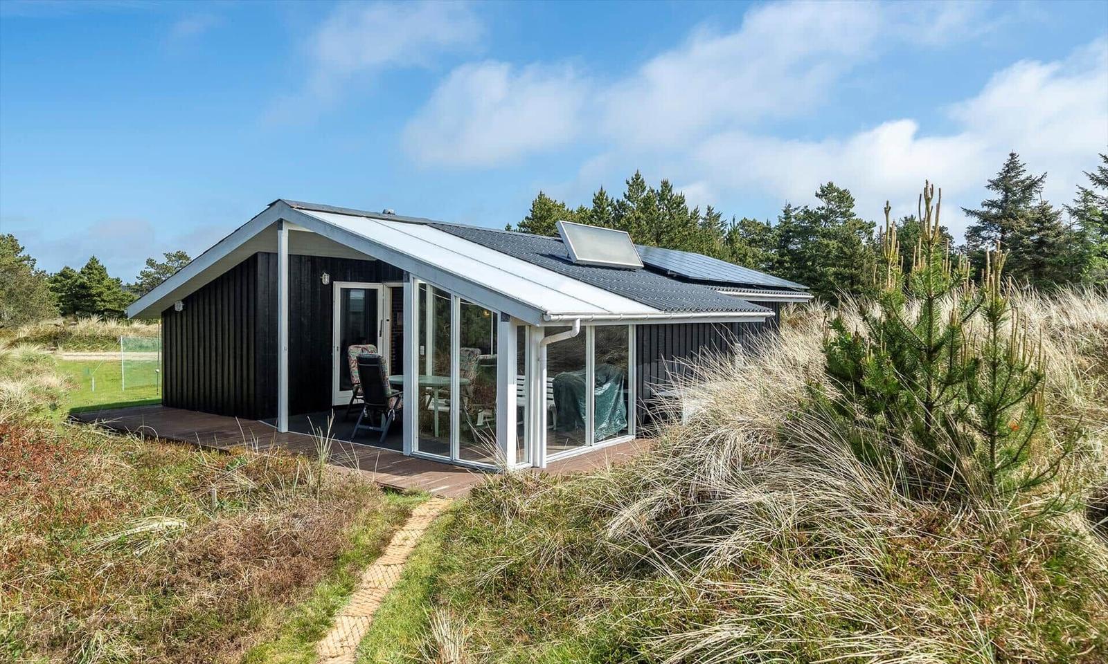 Moderne Hütte mit Terrasse und Solaranlage in grüner Umgebung.