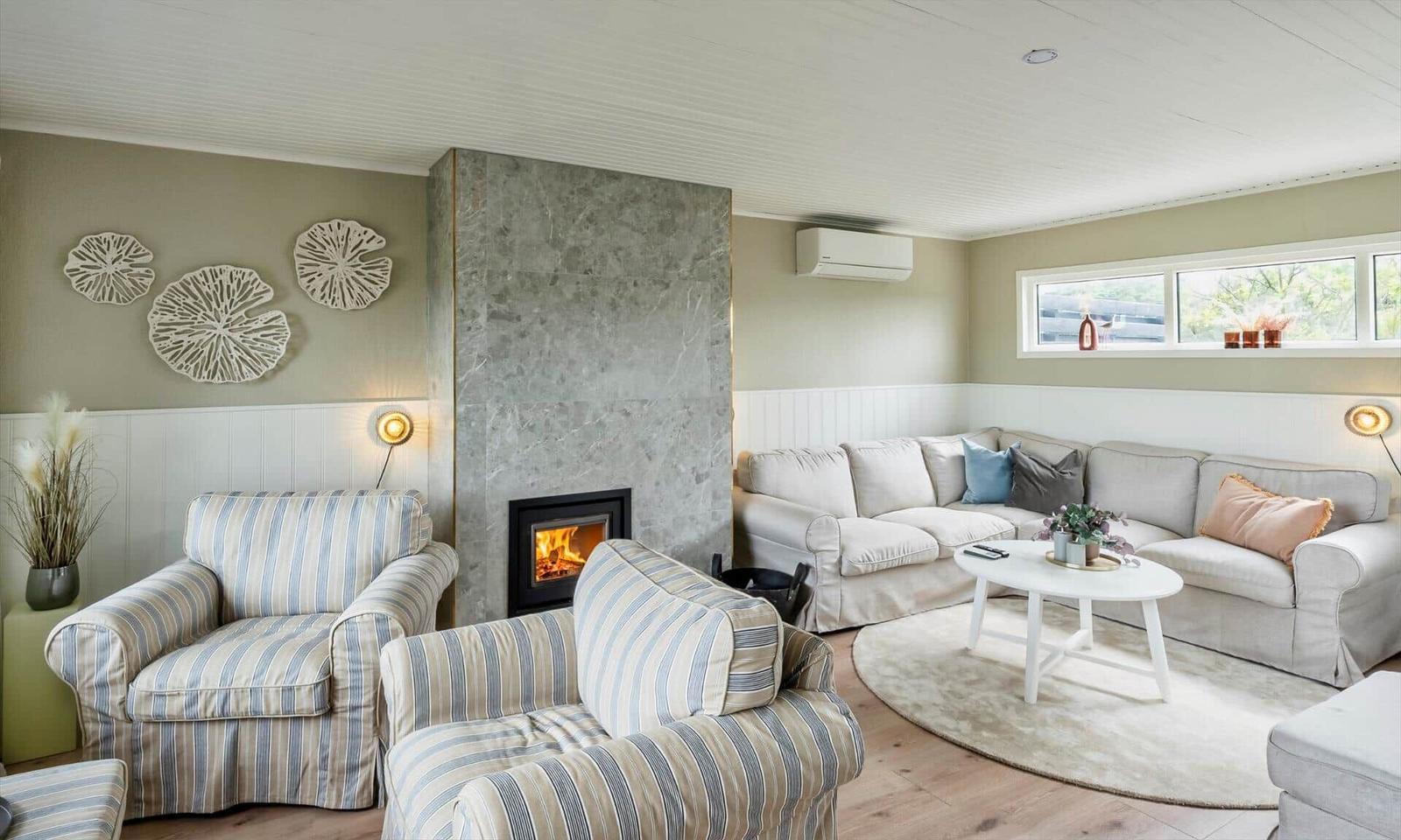 Living room with sofa, chairs, fireplace, and window. Wall decor and rug.