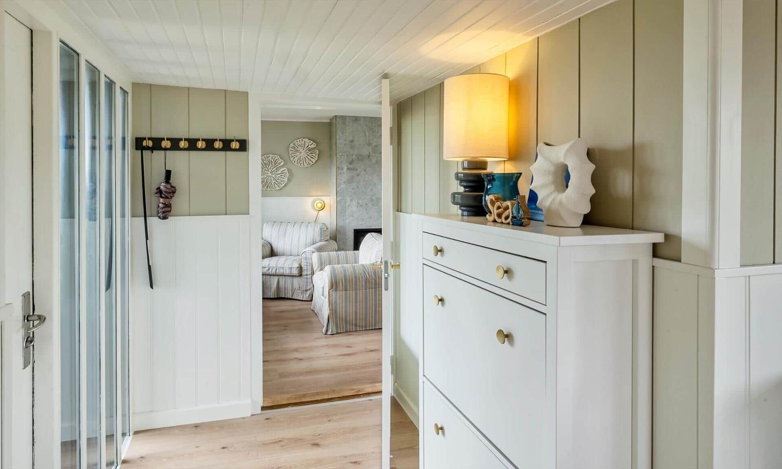 Entryway with cabinet, lamp, and decor. View into living room with seating.