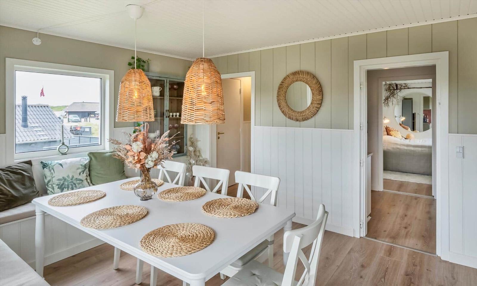 Dining room with white table, chairs, and rattan lamps. Hallway to bedroom with bed.