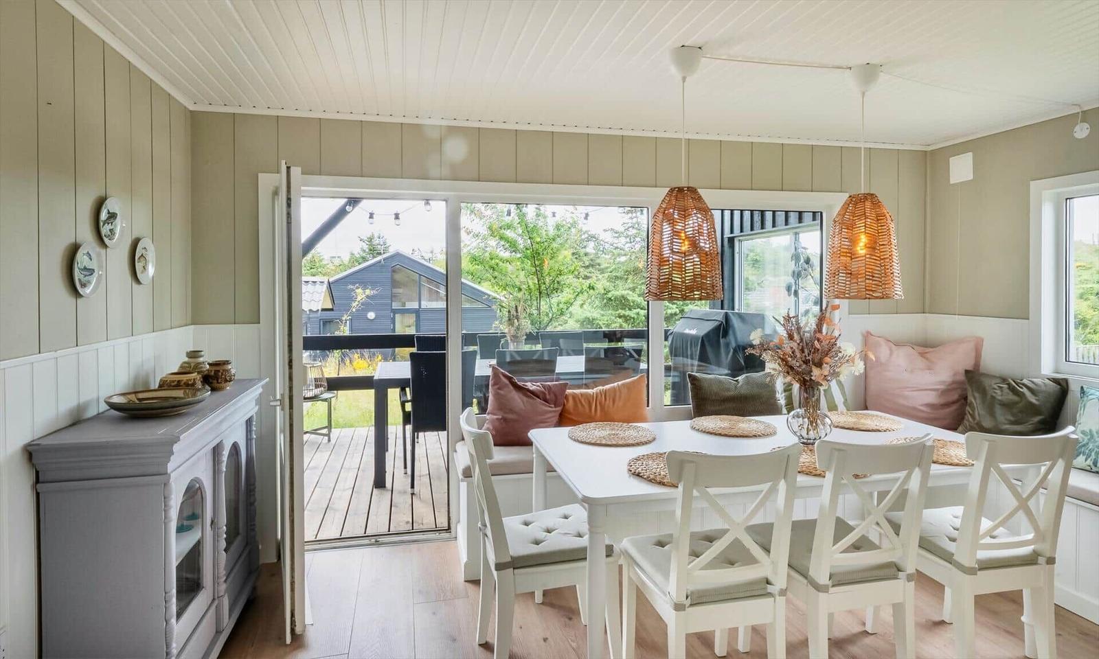 Dining room with white table, chairs, and bench. Entrance to terrace with garden view.