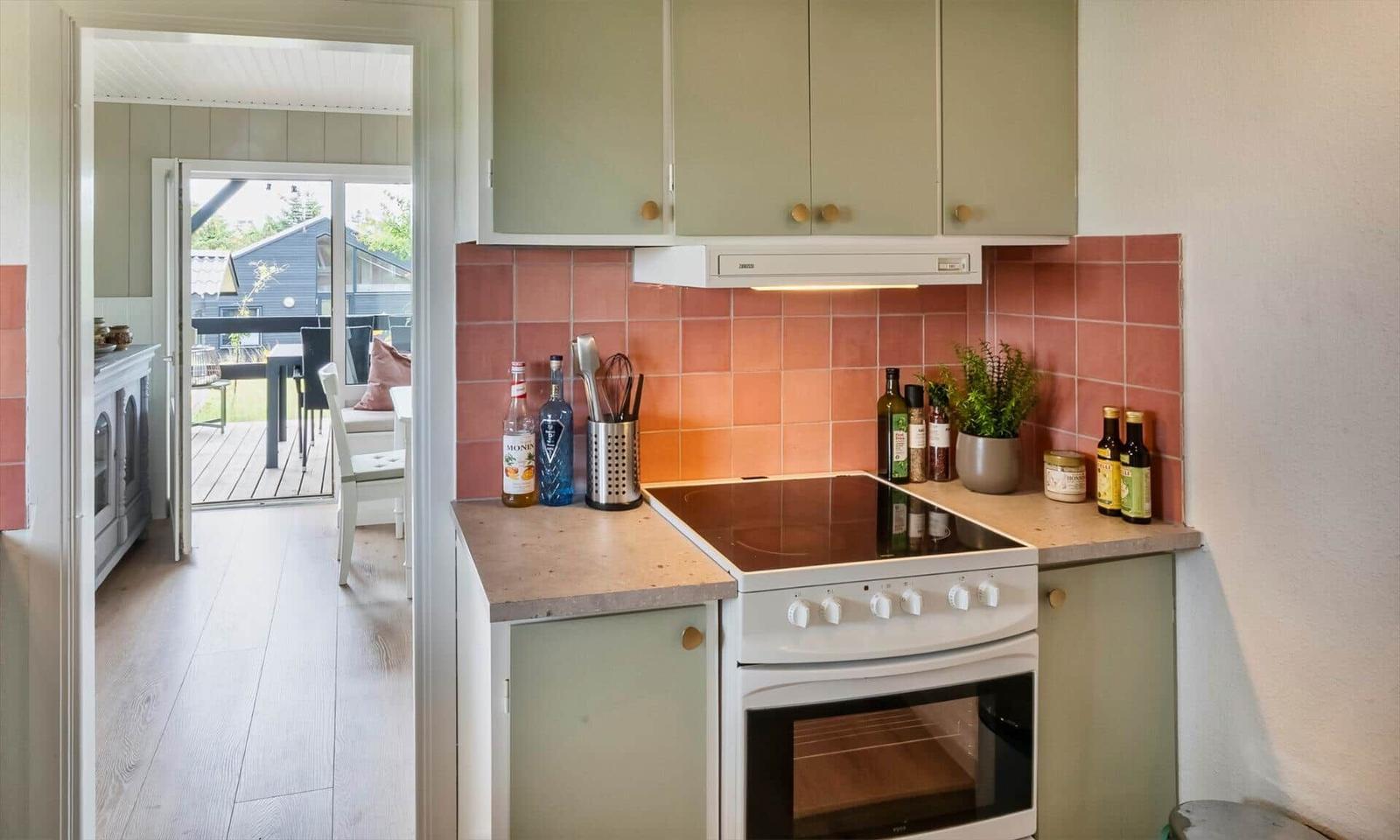 Kitchen with induction cooktop, wooden surfaces, and pink tiles on the wall.