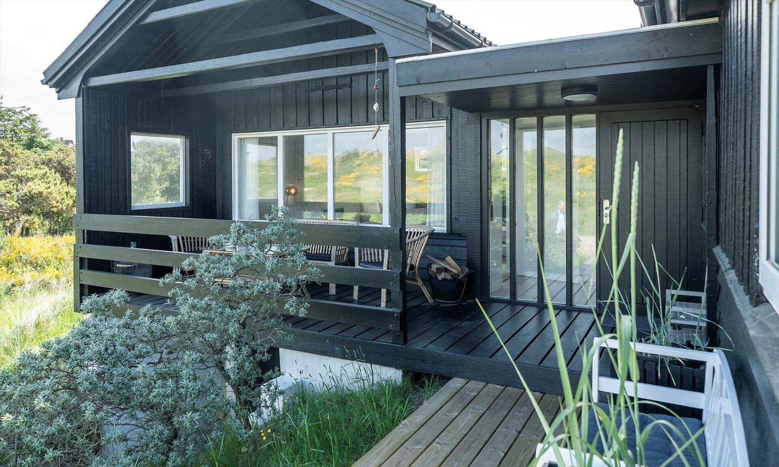 Black house with terrace and glass doors. Garden with plants and wooden steps.