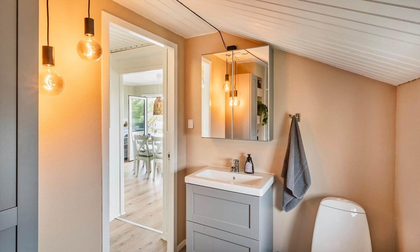 Bathroom with sink, mirror, and toilet. Corridor to kitchen with table and chairs.