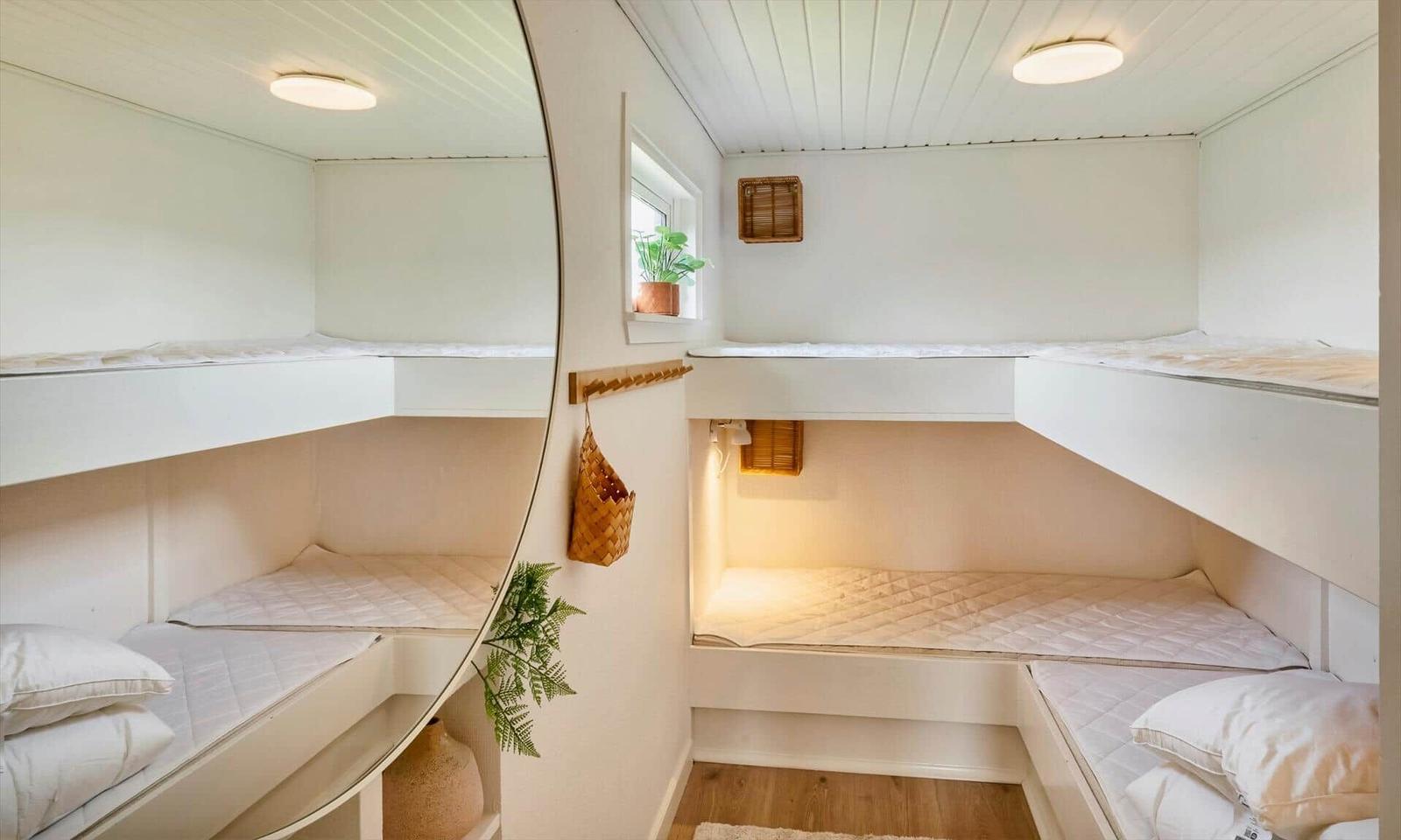 Two bunk beds with mattresses and pillows in a bright room with wooden floor and window.