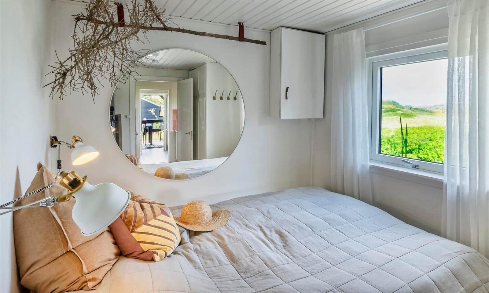 Bedroom with bed, wall mirror, and window view of green field.