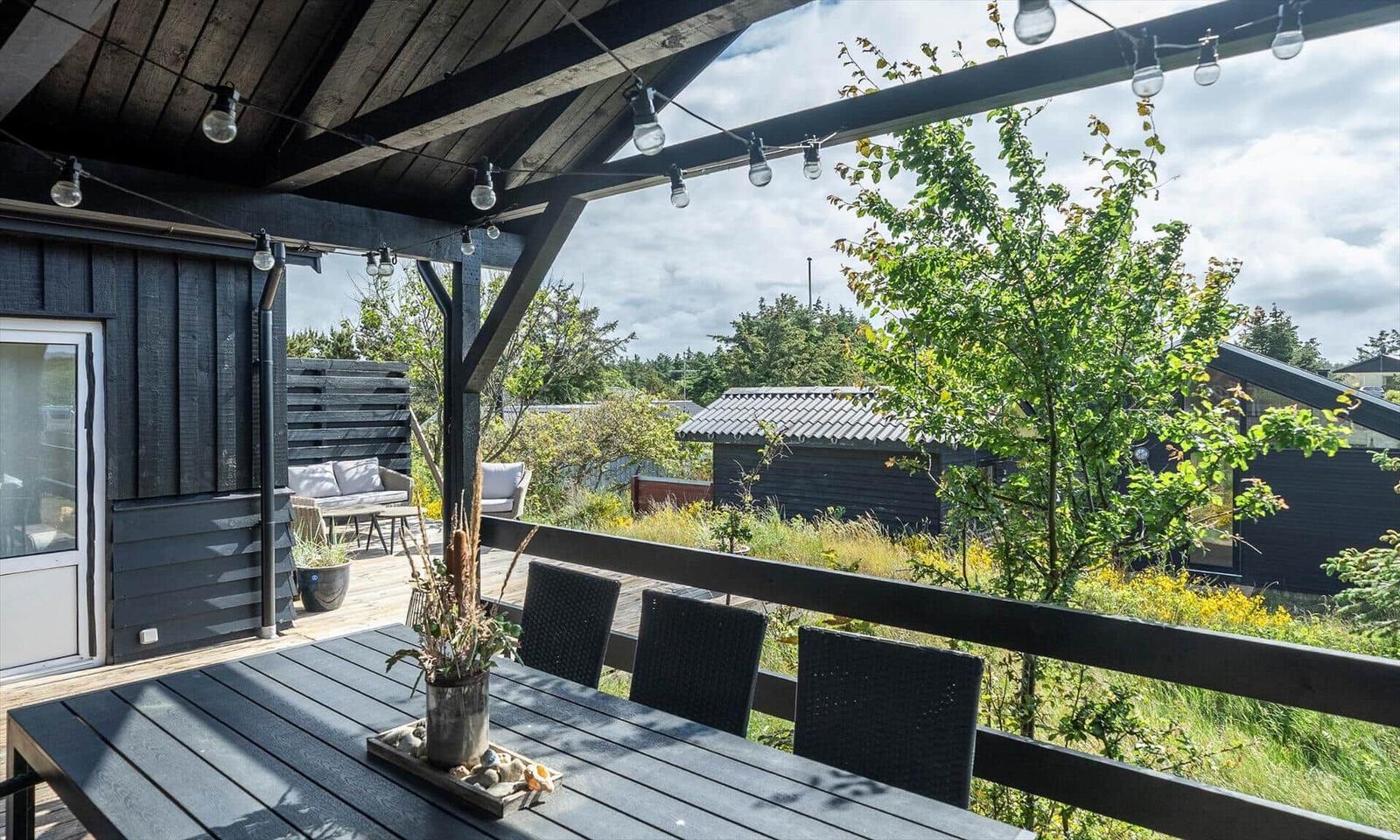 Terrace with table, chairs, and string lights. View of green trees and neighboring houses.