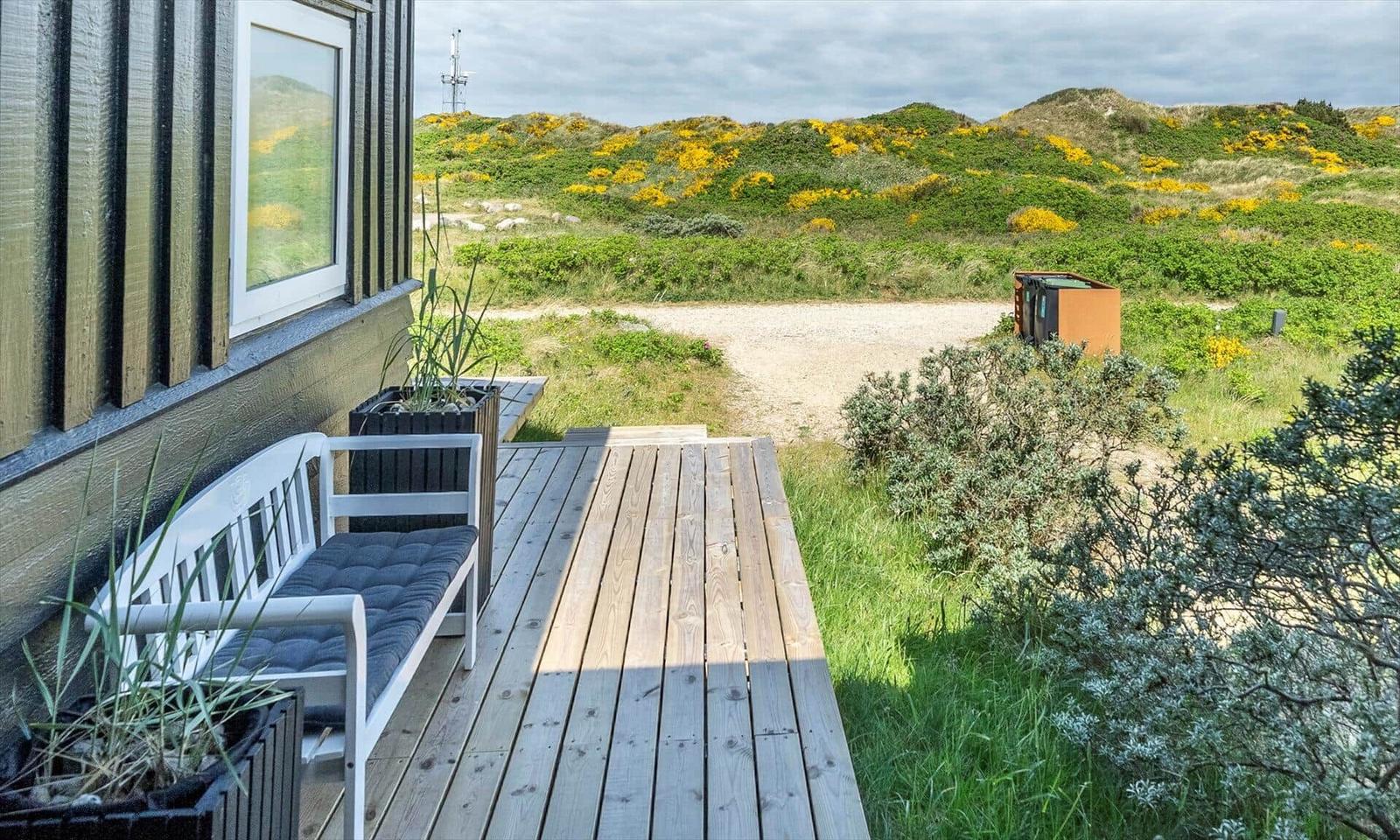 Deck with white chair and wooden floor. View of green hills with yellow flowers.