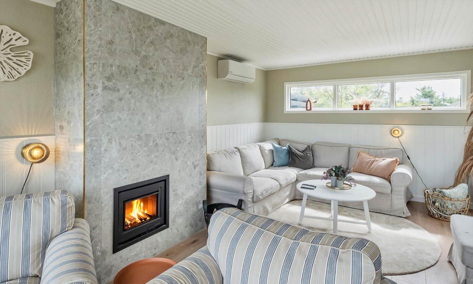 Living room with fireplace, sofa, and table. Windows and wainscoting visible.