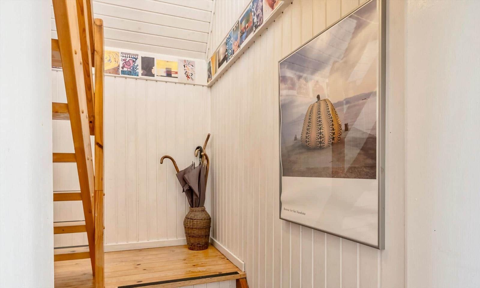 Helle Wand mit Bild und Regal. Holztreppe und Korb mit Regenschirmen.