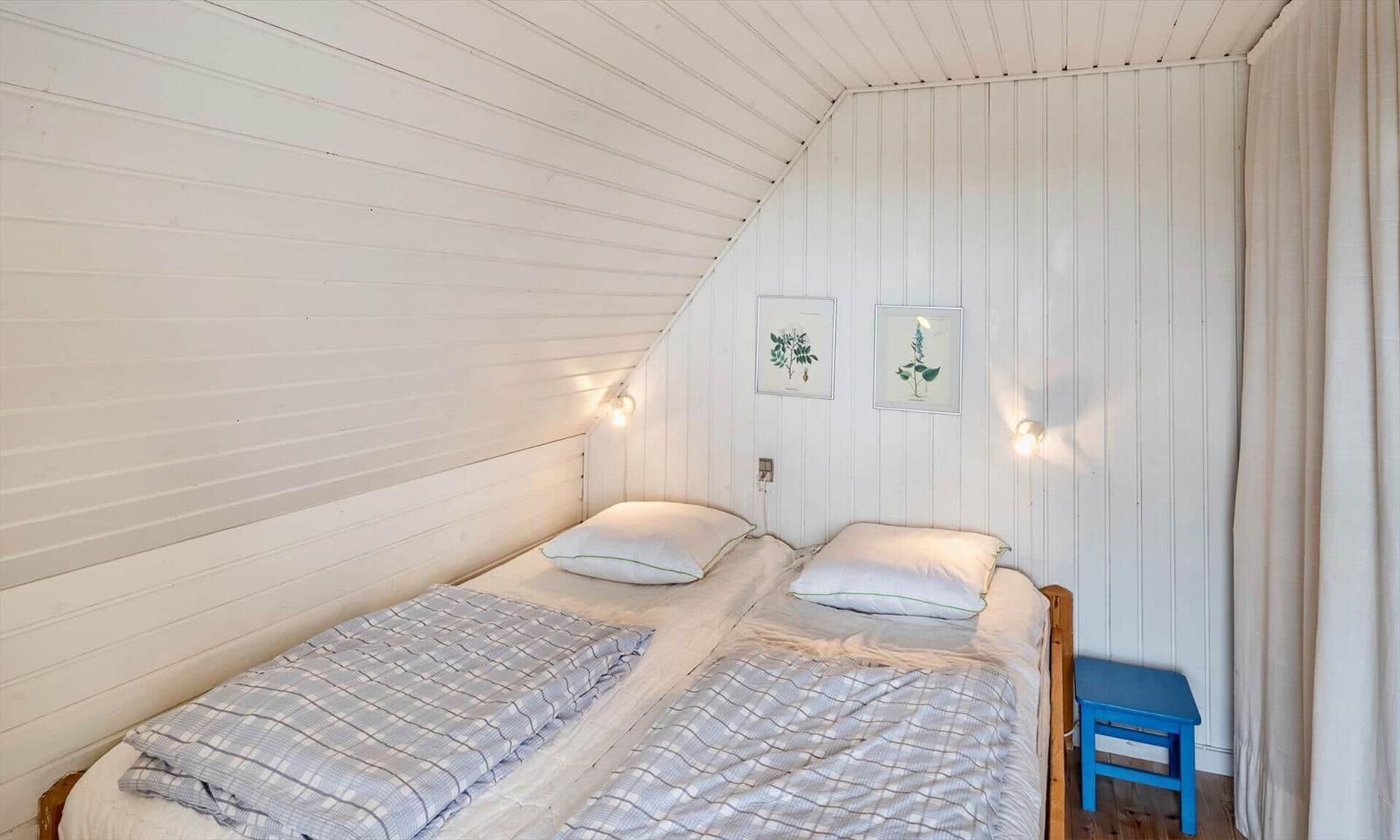 Zimmer mit Doppelbett, weißen Wänden und zwei Wandlampen. Blauer Stuhl und Vorhang sichtbar.