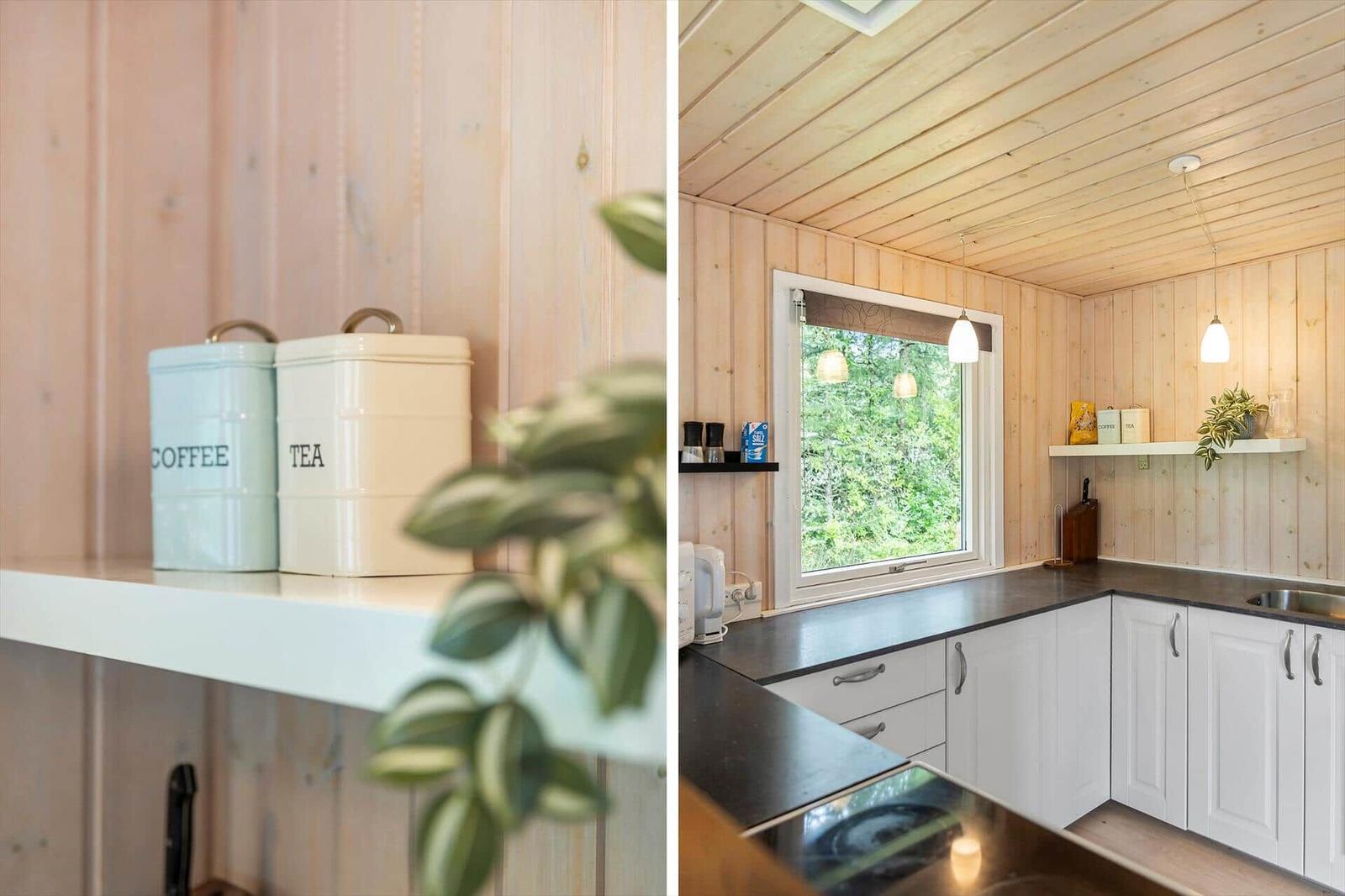 Küche mit Holzwand, weißen Schränken und Fenster mit Blick auf Wald.