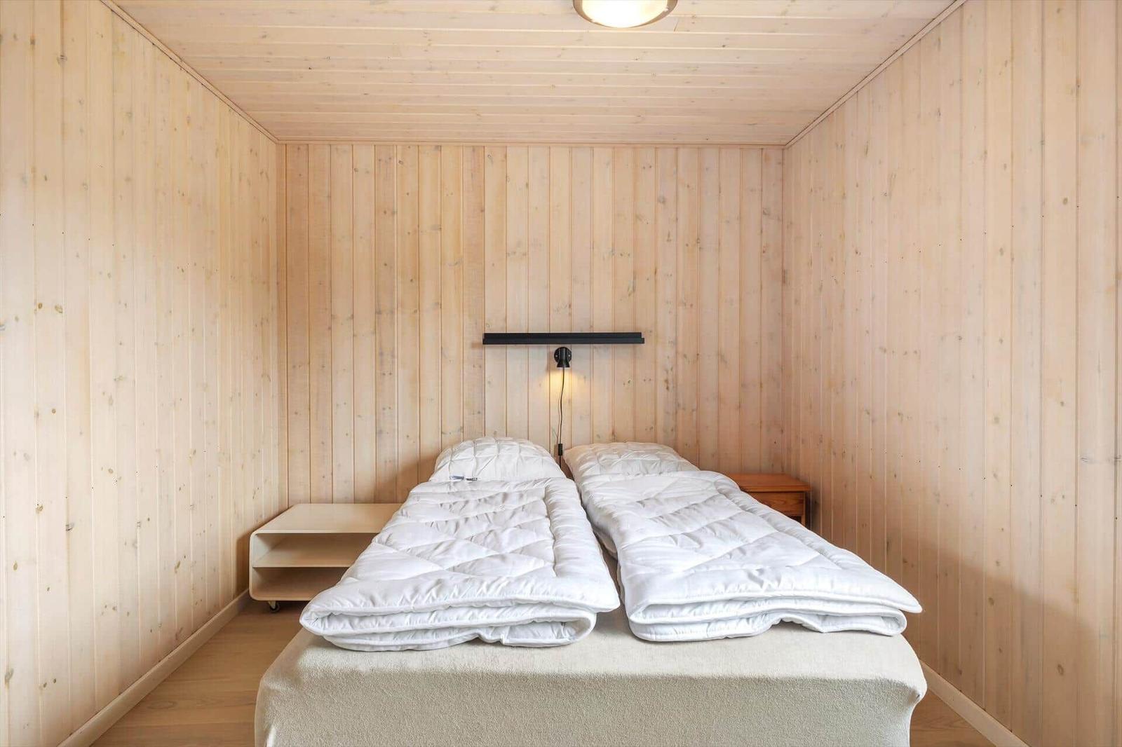 Zwei Betten mit weißen Decken in einem Holzraum mit Wandlampe.