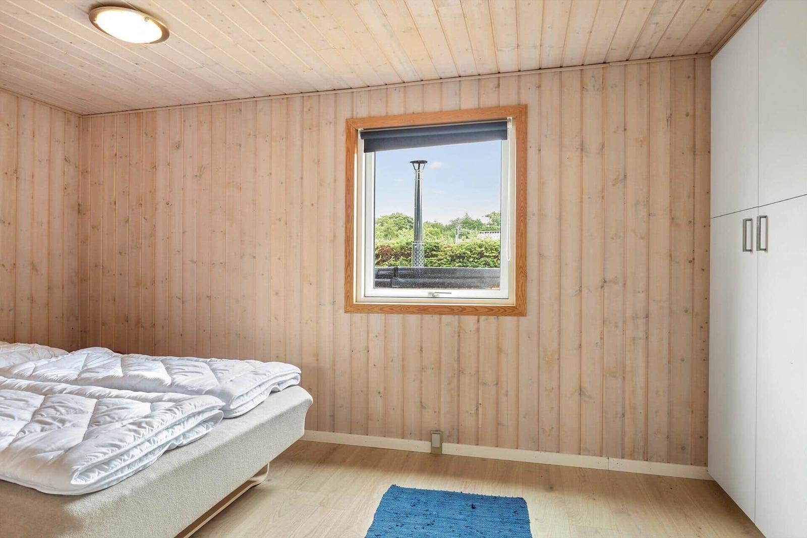 Schlafzimmer mit Holzwandverkleidung, Bett, Fenster und Schrank.