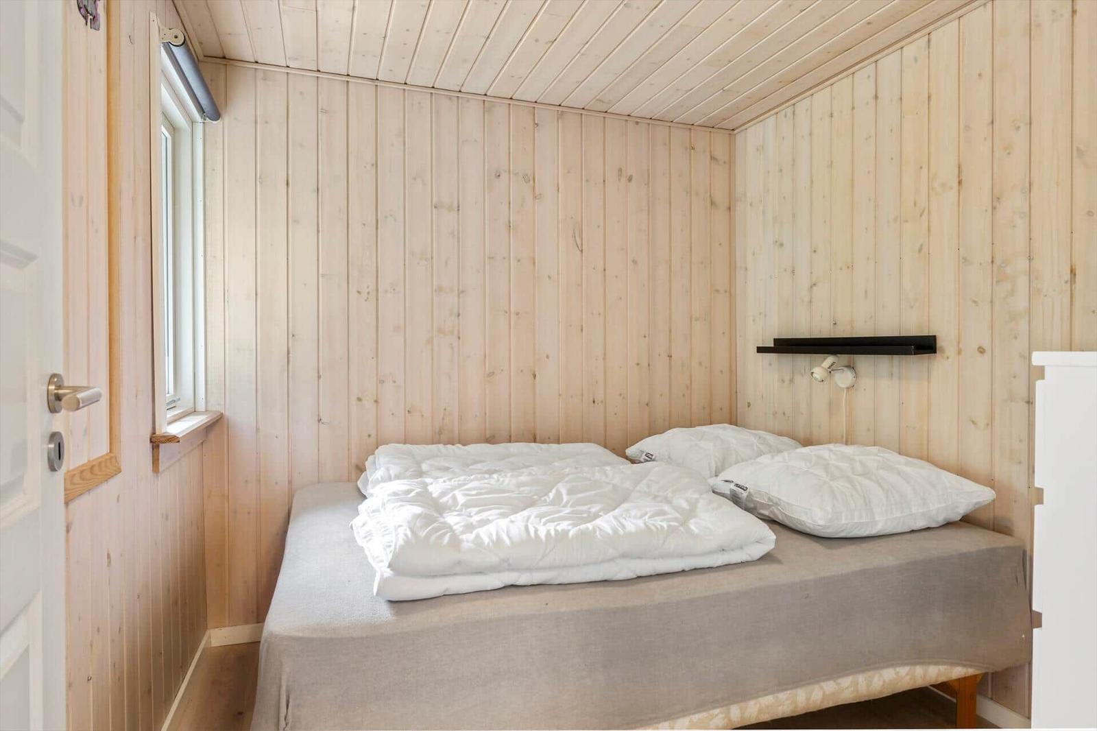 Ein Schlafzimmer mit Holzwänden, einem Bett mit weißer Bettwäsche und einem Fenster.