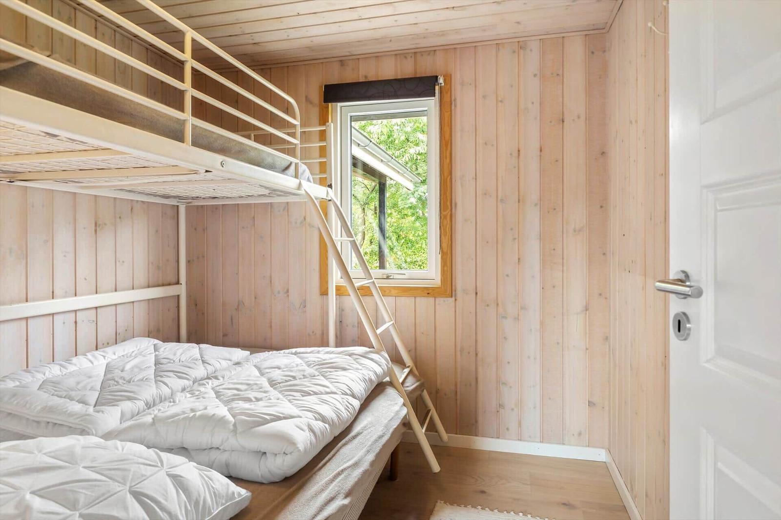 Schlafzimmer mit Doppelbett und obere Schlafcouch, Holzwand und Fenster mit Blick auf Bäume.