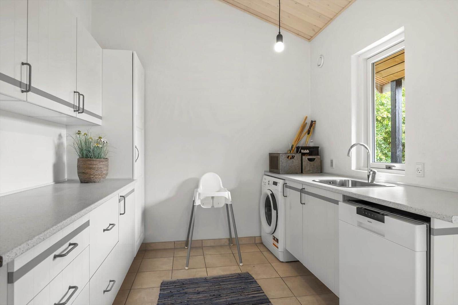 Küche mit Waschmaschine, Spüle und Hochstuhl. Fenster mit Blick auf Grün.