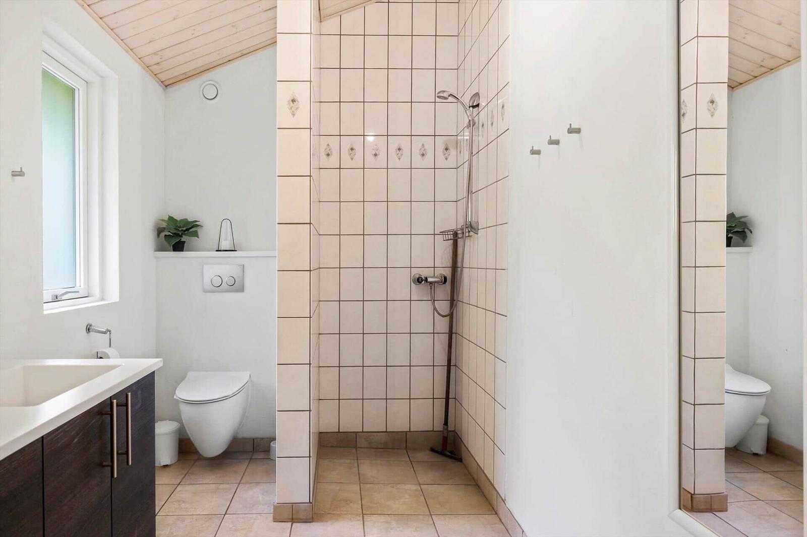 Badezimmer mit Dusche, Toilette und Waschbecken. Holzdecke und Fliesen.