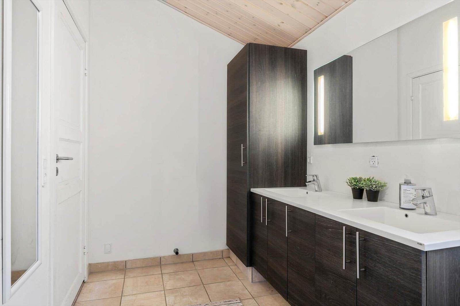 Badezimmer mit zwei Waschbecken, dunklen Schränken und beleuchtetem Spiegel.