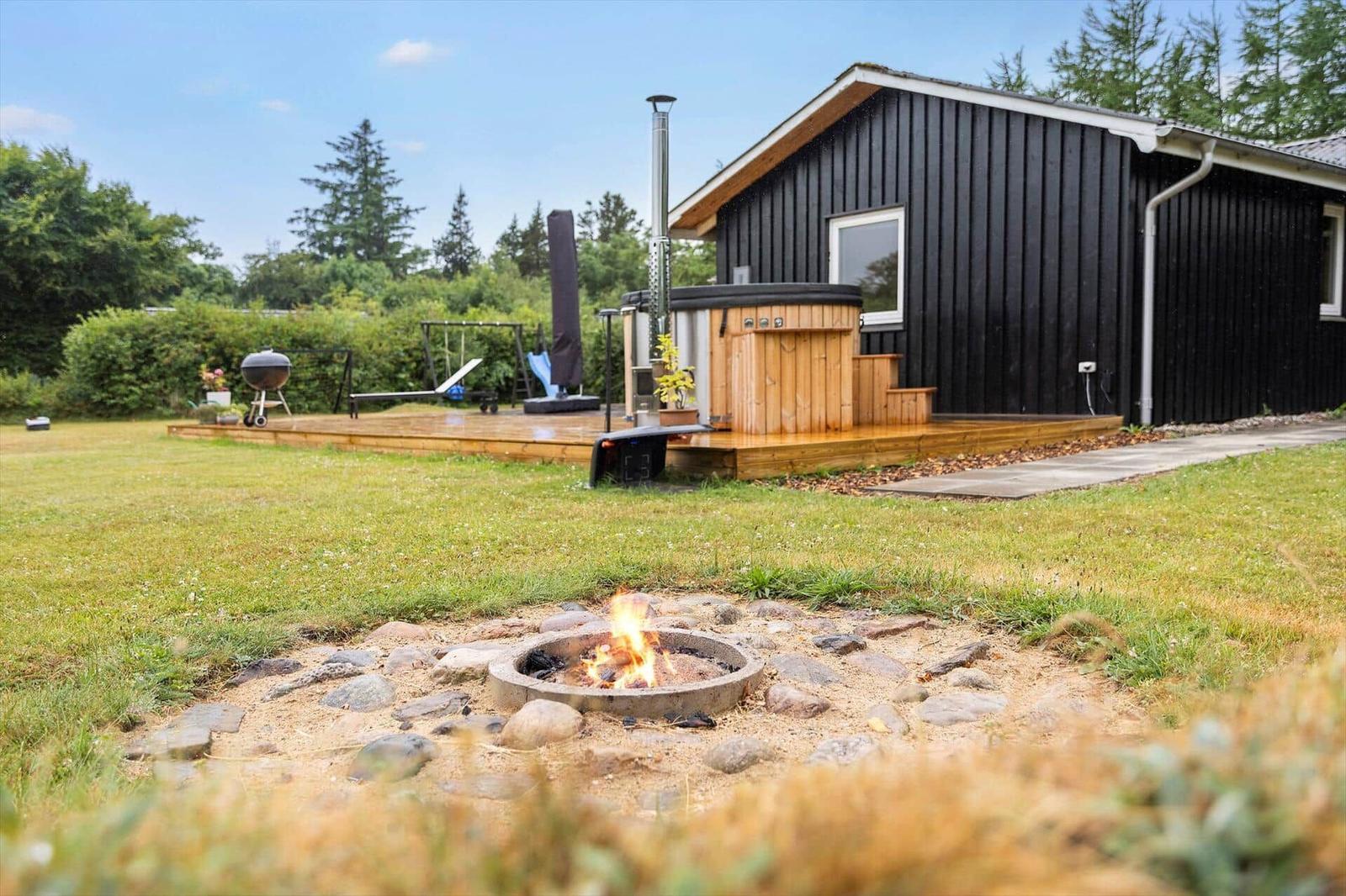 Haus mit Holzterrasse, Whirlpool und Feuerkorb im Garten.