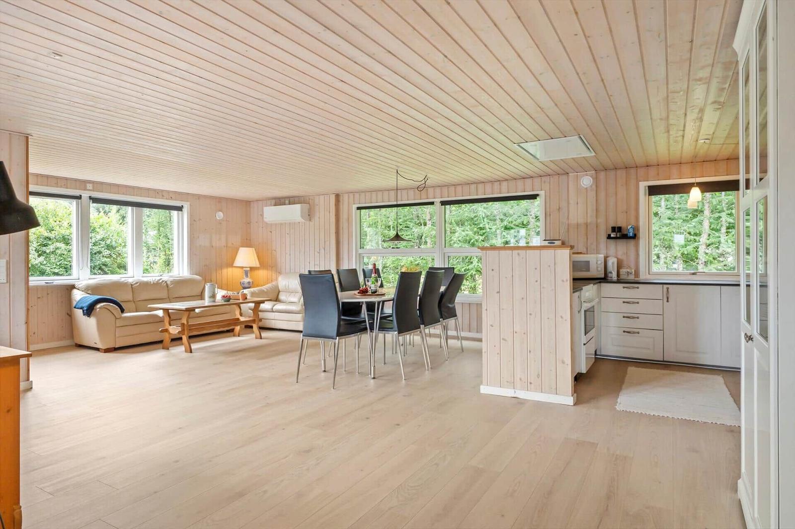 Wohn- und Essbereich mit Holzdecke, Sofa, Tisch und Küchenzeile.