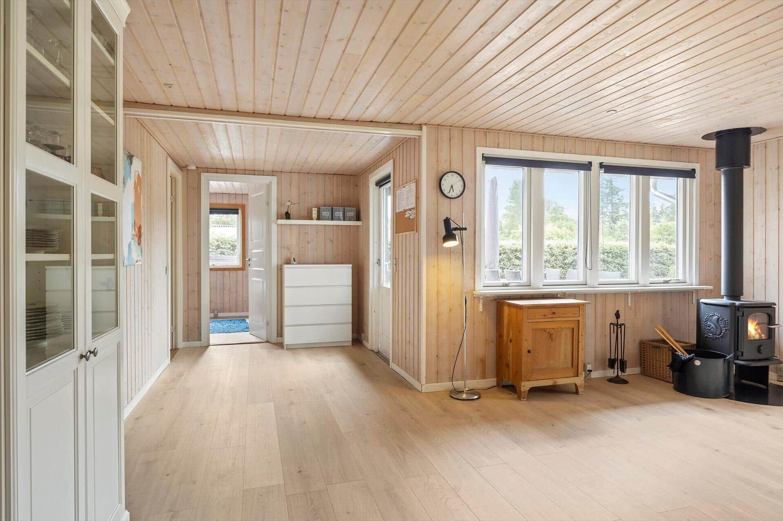 Holzvertäfelte Wohnung mit Kaminofen, Fenster und Schrank.