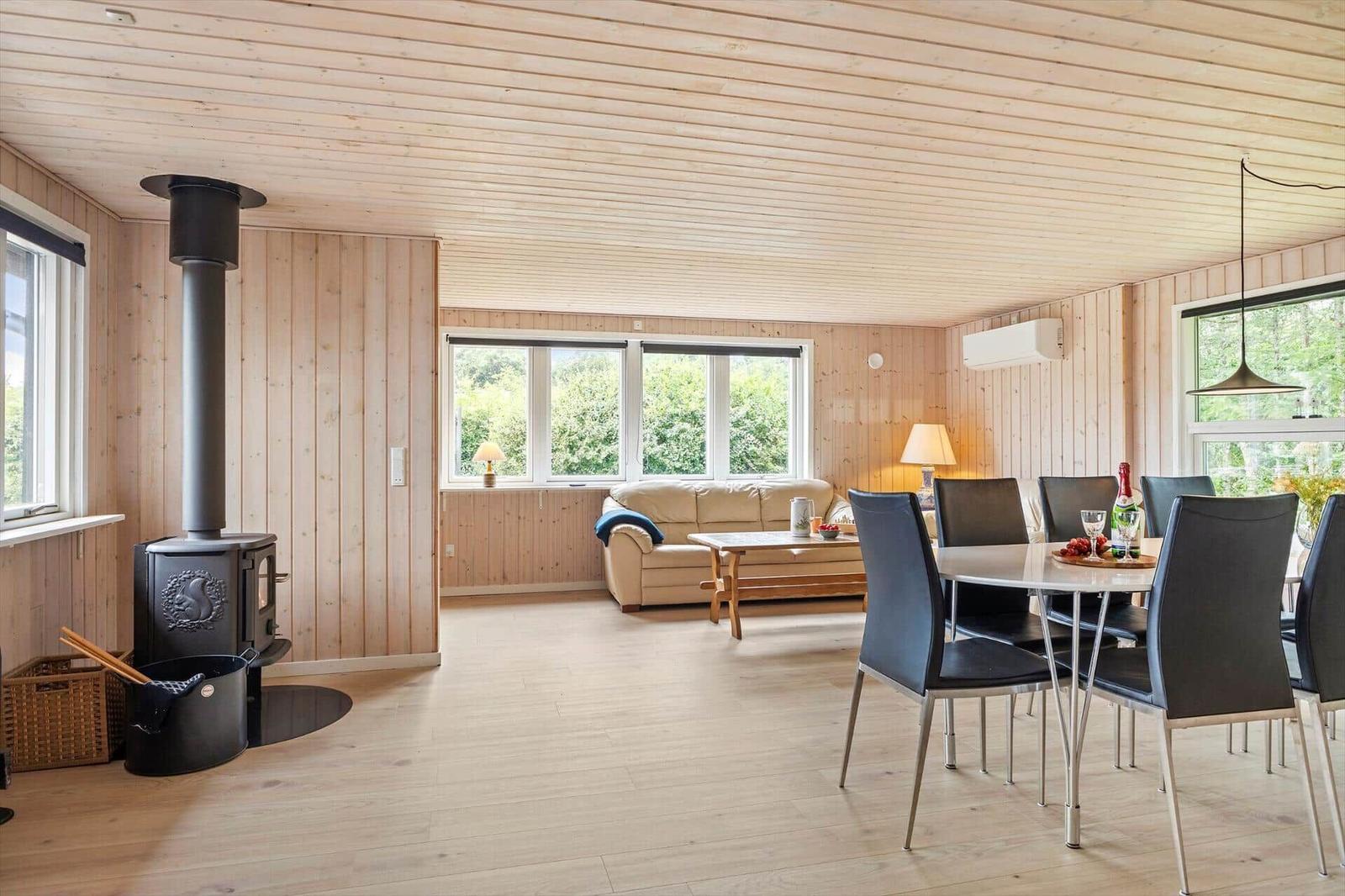Wohn- und Essbereich mit Holzwand, Kaminofen und Fenstern zum Garten.
