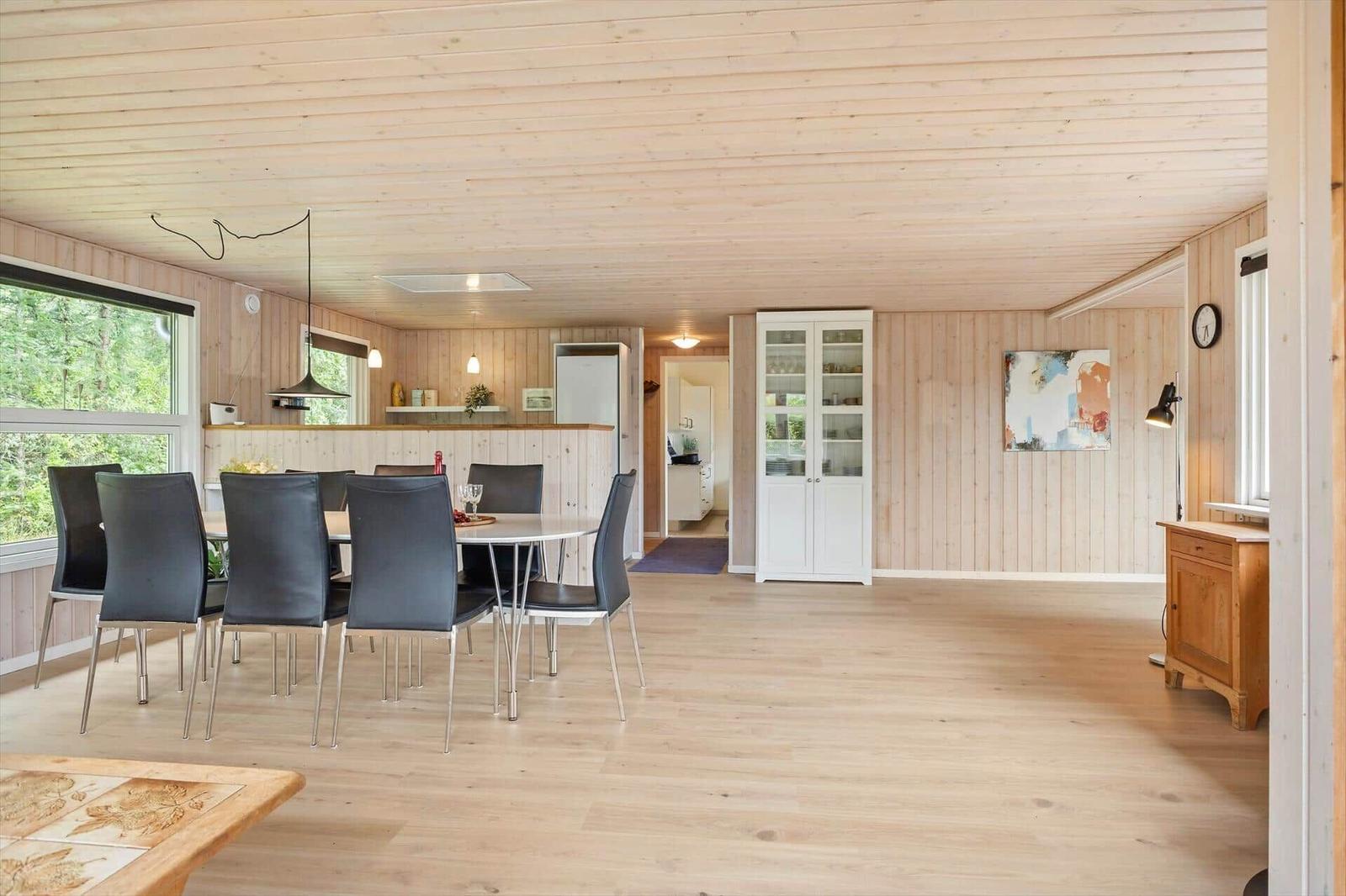 Essbereich mit Tisch und Stühlen, Holzwände und -boden, Küchenbereich im Hintergrund.