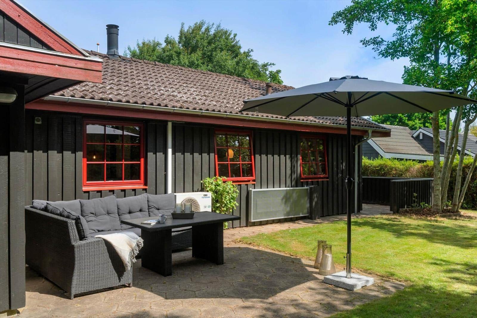 Terrace with seating, sunshade, and lawn in front of a house with red window frames.