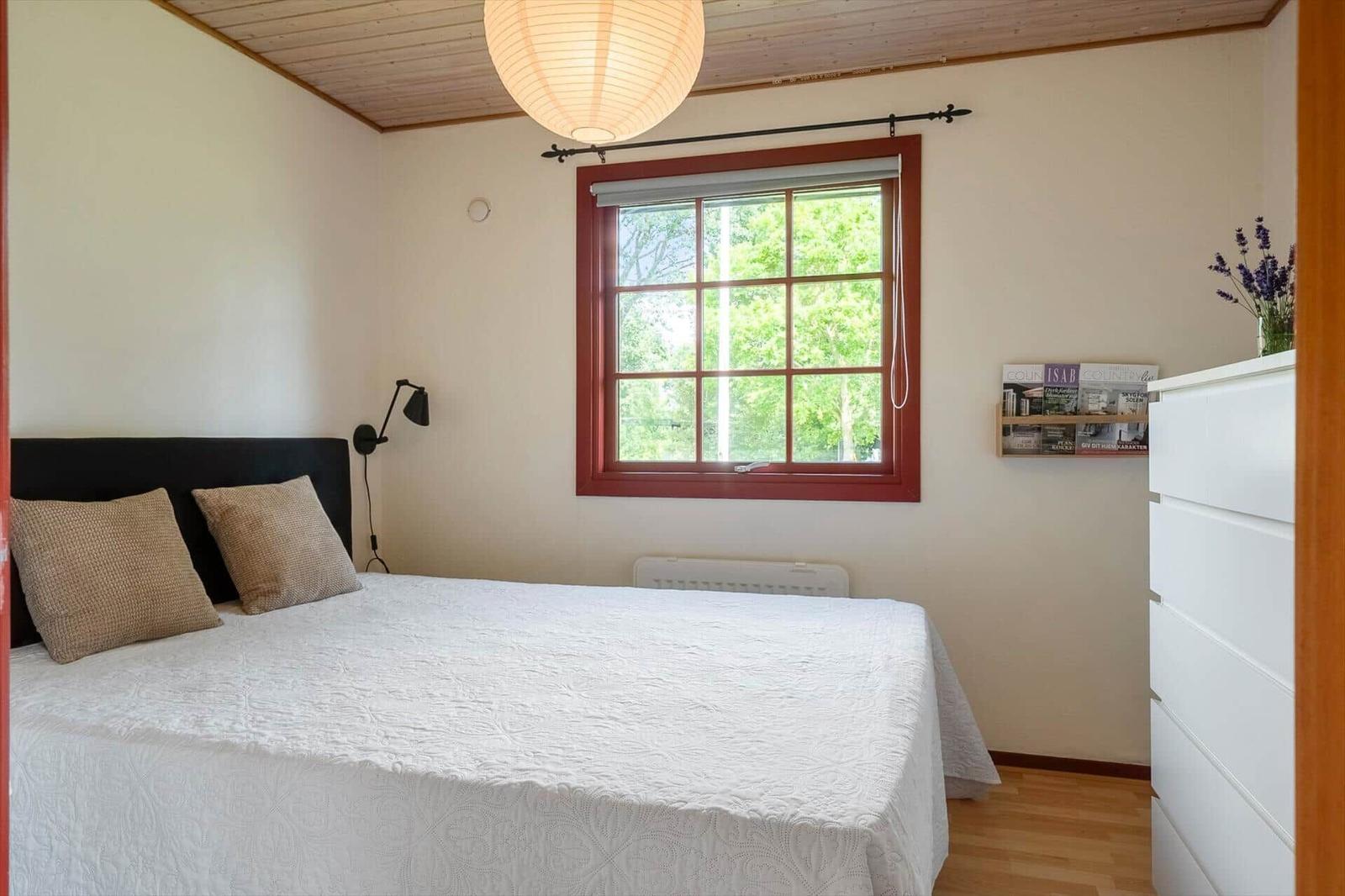 Bedroom with bed, window, and dresser. Wooden ceiling, lamp, and wall mount.