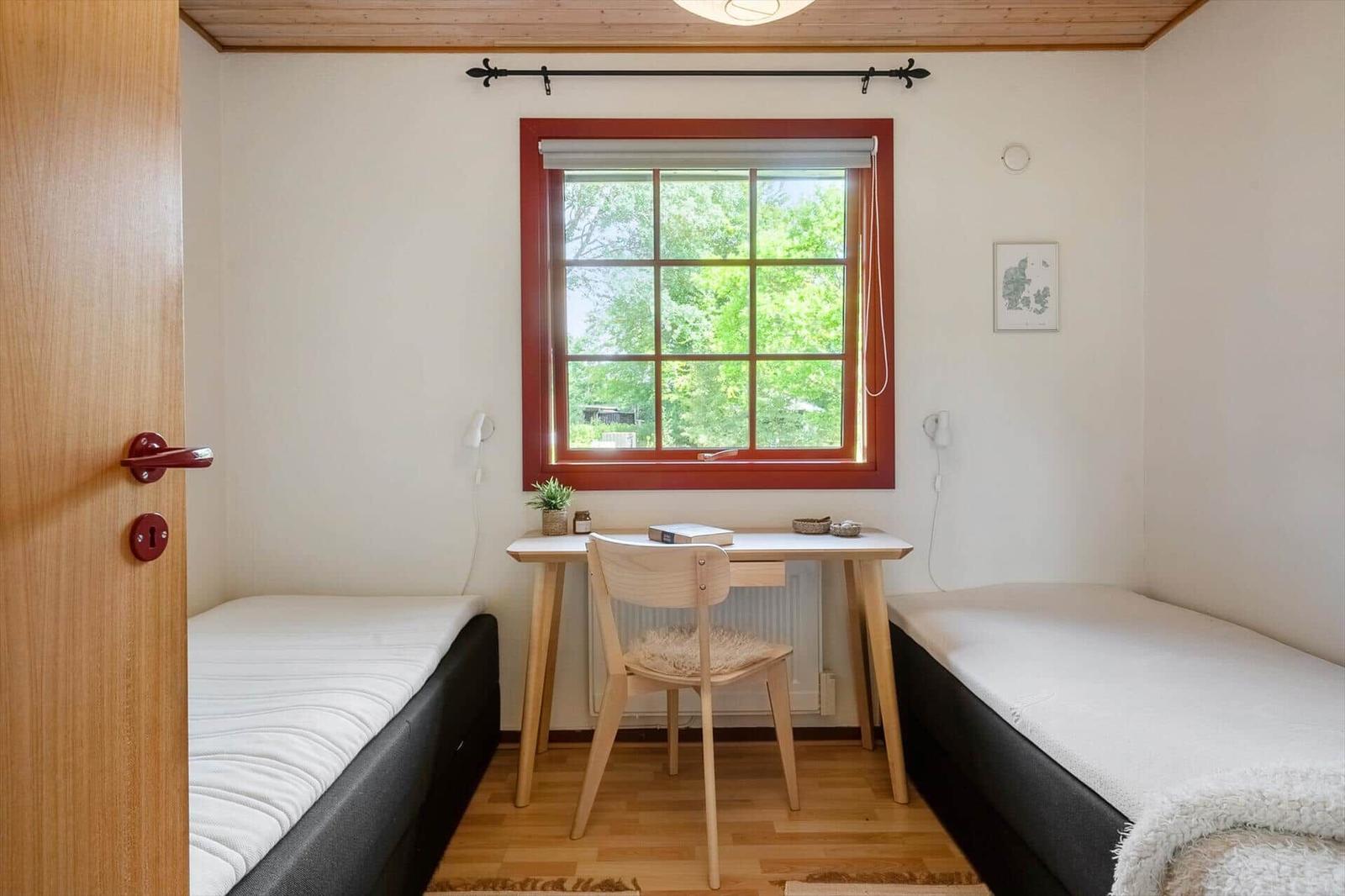 Room with two beds, desk, and window with view of green.