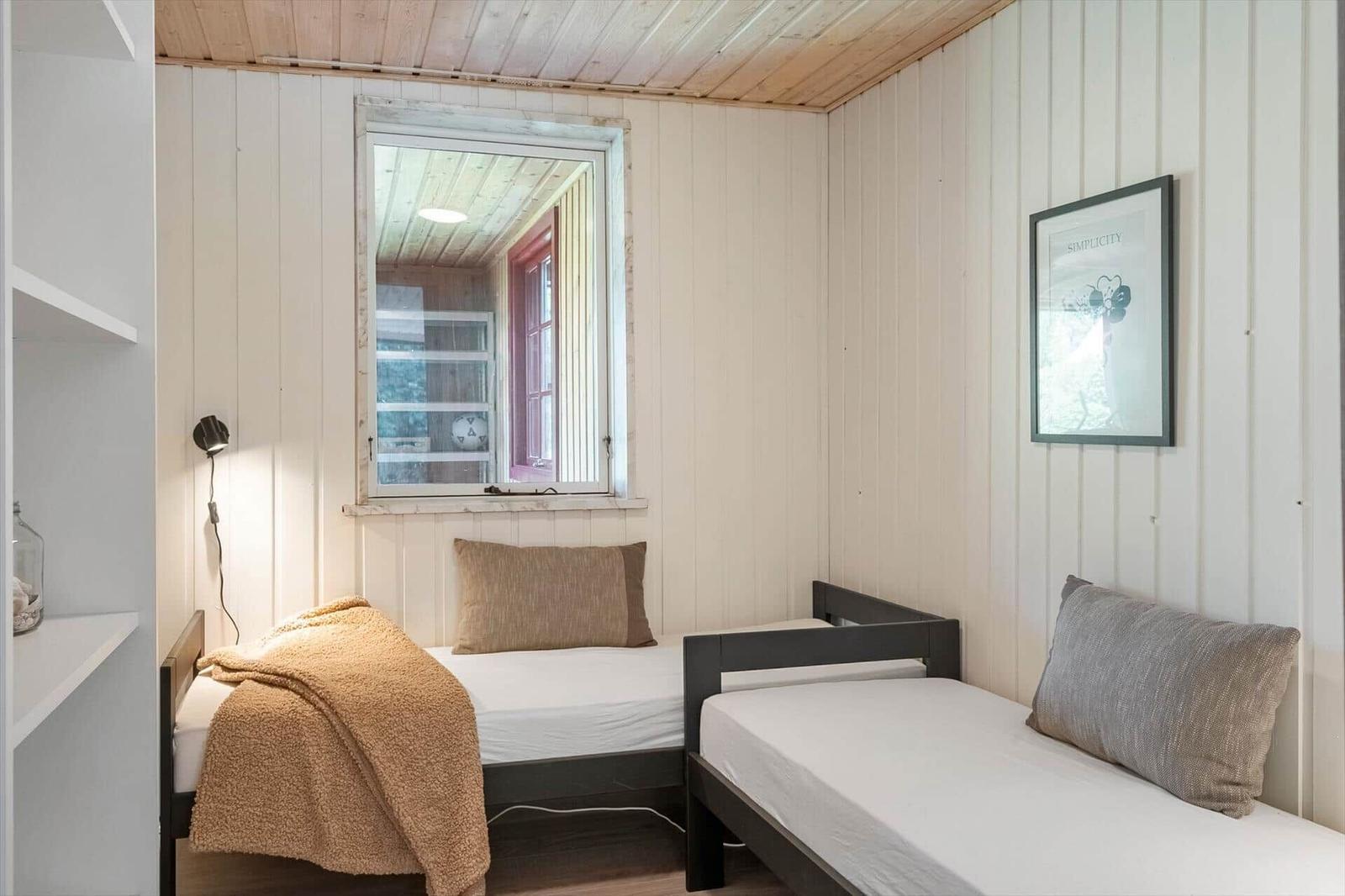 Two single beds in a room with wood paneling and a window.