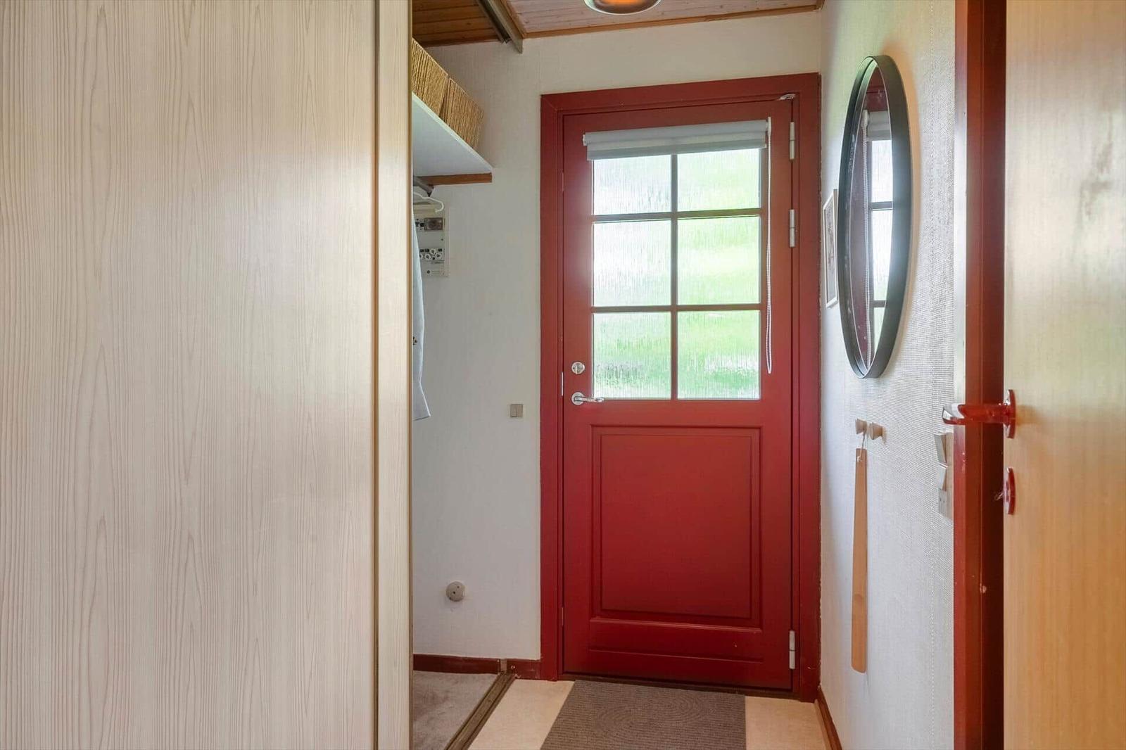 Red door with glass pane, mirror, and coat rack in hallway.