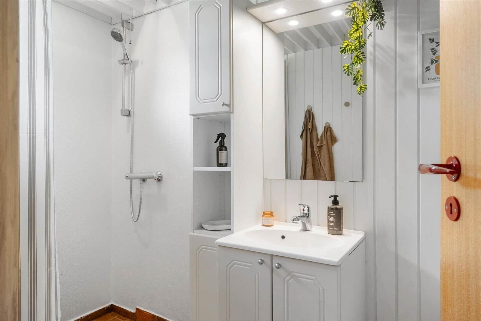 Shower, sink, and mirror cabinet in white bathroom fixtures.