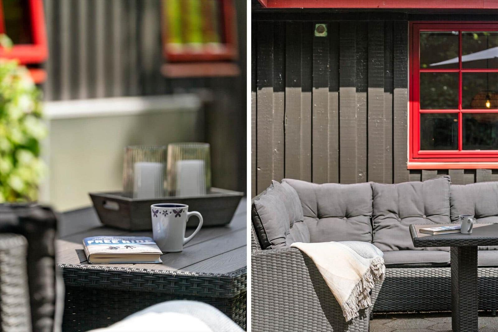 Outdoor seating area with table, book, and mug. Red window and wooden wall in background.