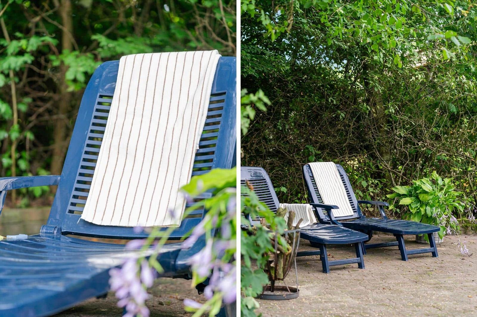 Two blue lounge chairs with towels in the garden, surrounded by greenery and flowers.