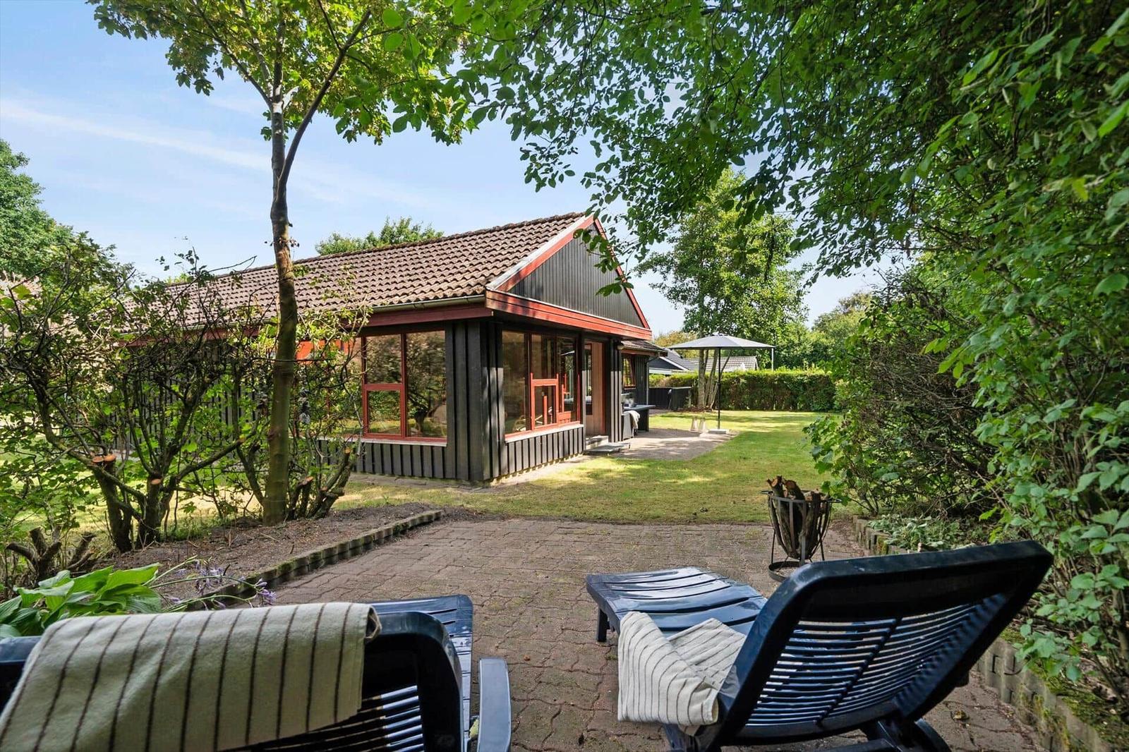 House with garden, terrace and loungers under trees.