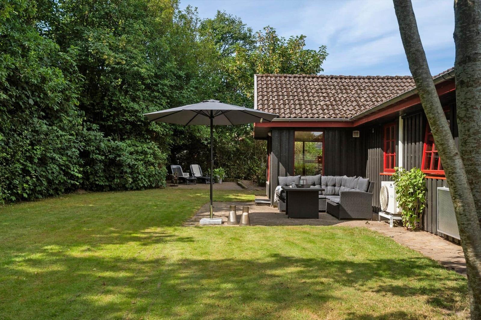 Backyard with garden, seating area, and umbrella next to a house with red windows.