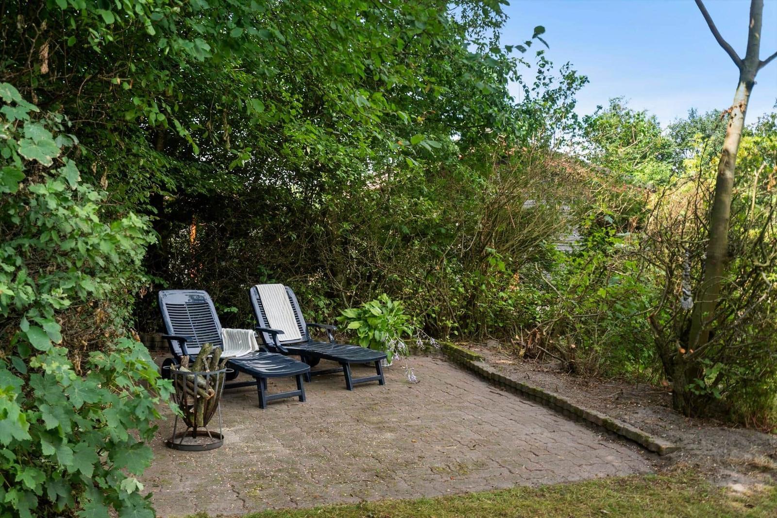 Two lounge chairs are on a paved area in the greenery.