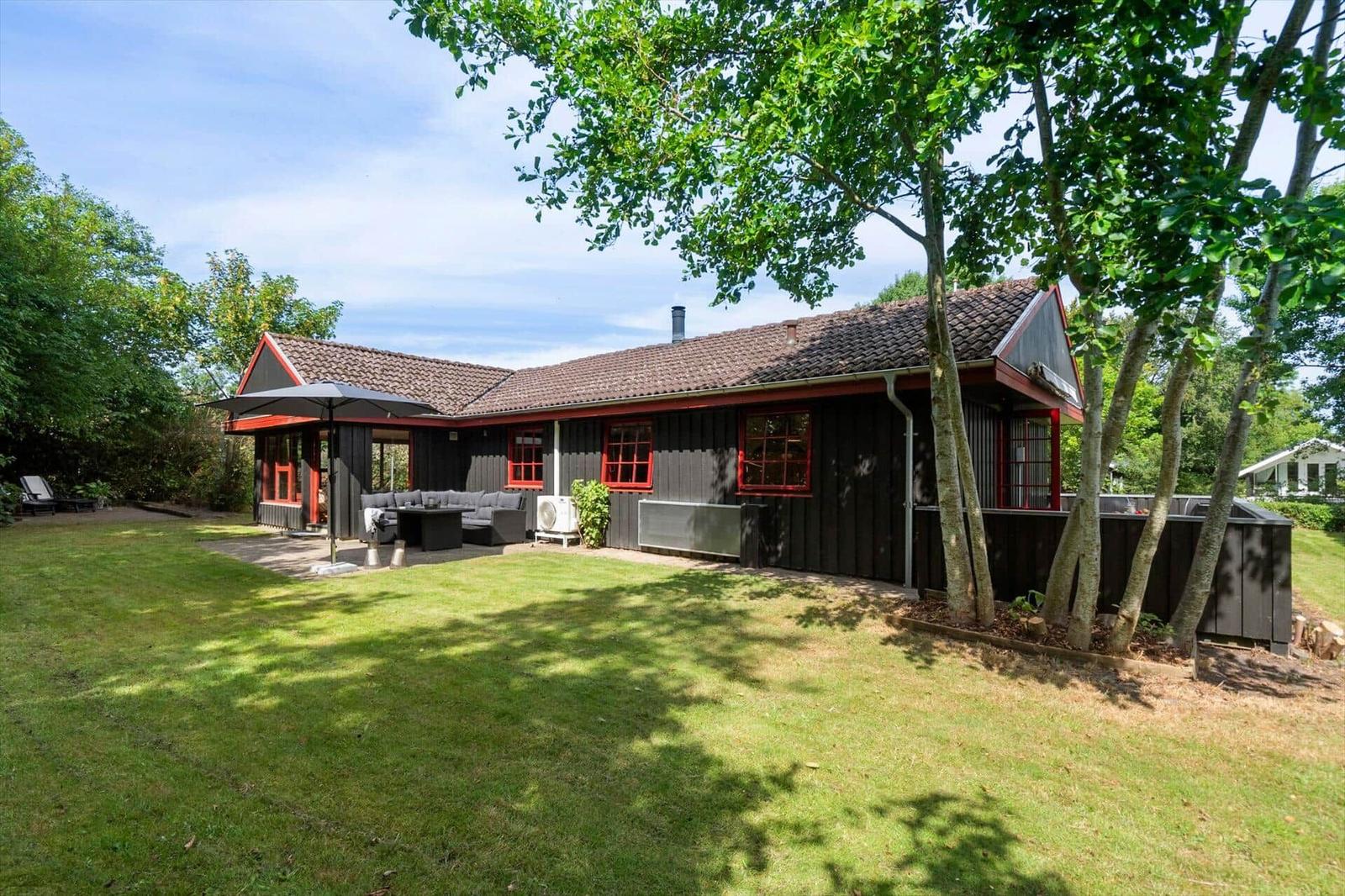 Wooden house with red window frames, terrace, and garden under trees.