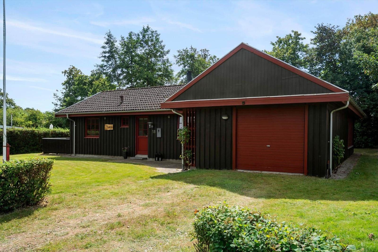 A house with a red garage and dark facade. Lawn and trees surround the building.