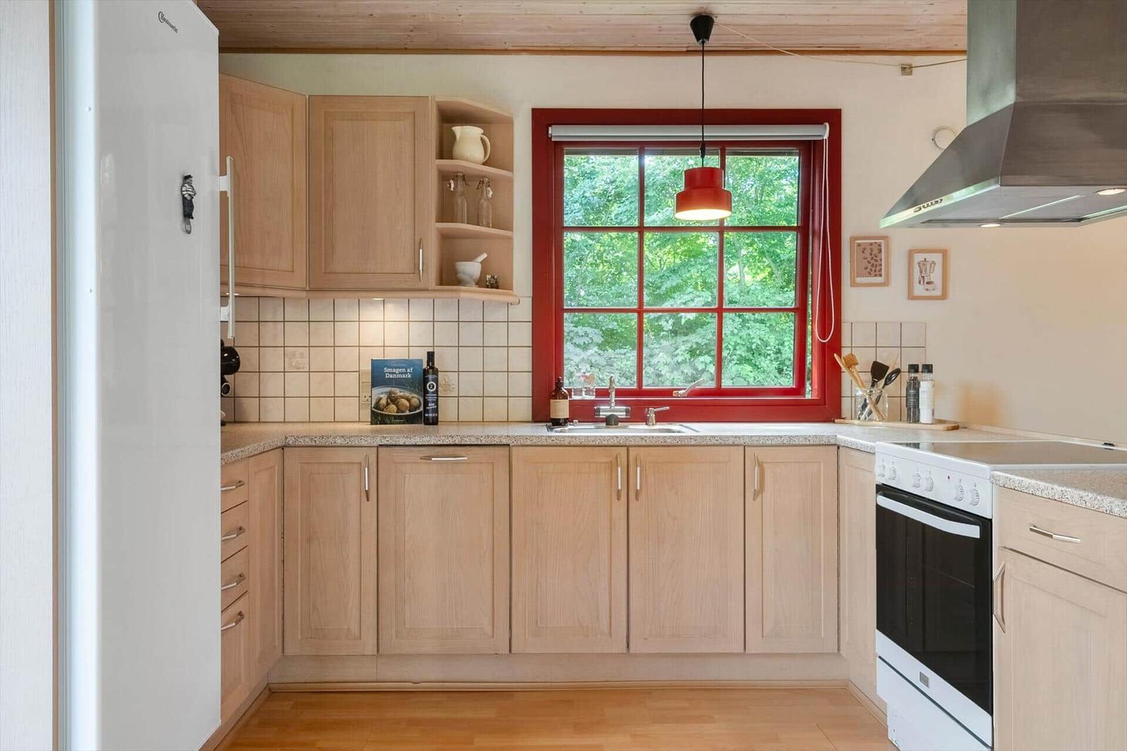 Kitchen with wooden cabinets, red window frame, and view of greenery.