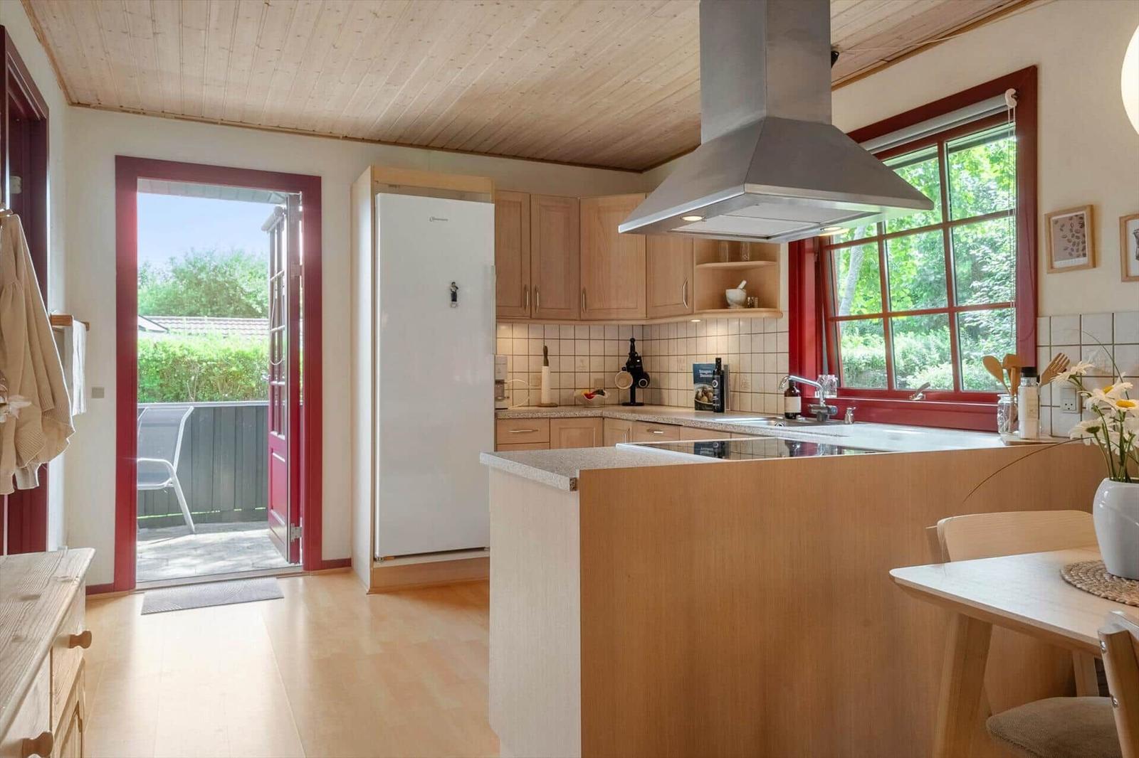 Kitchen with wooden surfaces, white cabinets, and red window frames. Entrance to the terrace.
