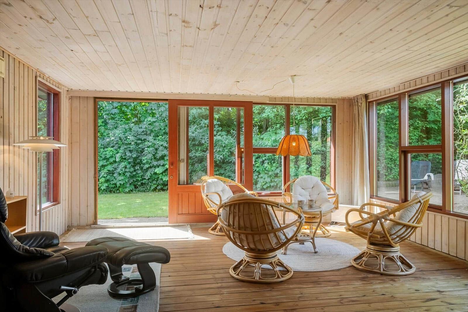 Living room with wooden ceiling, rattan chairs, and view of green garden.