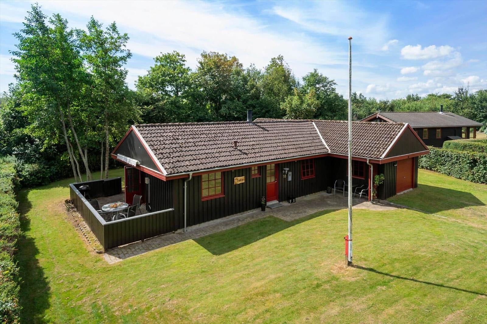 A dark brown holiday home with red window frames and a terrace in the green.