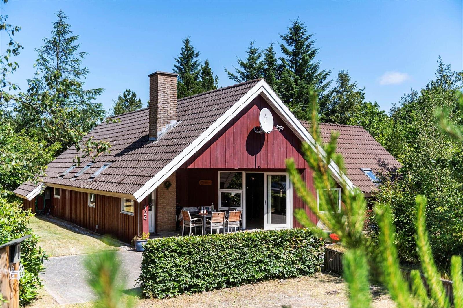 Rotes Holzhaus mit Terrasse, Grillplatz und Satellitenschüssel in grüner Umgebung.