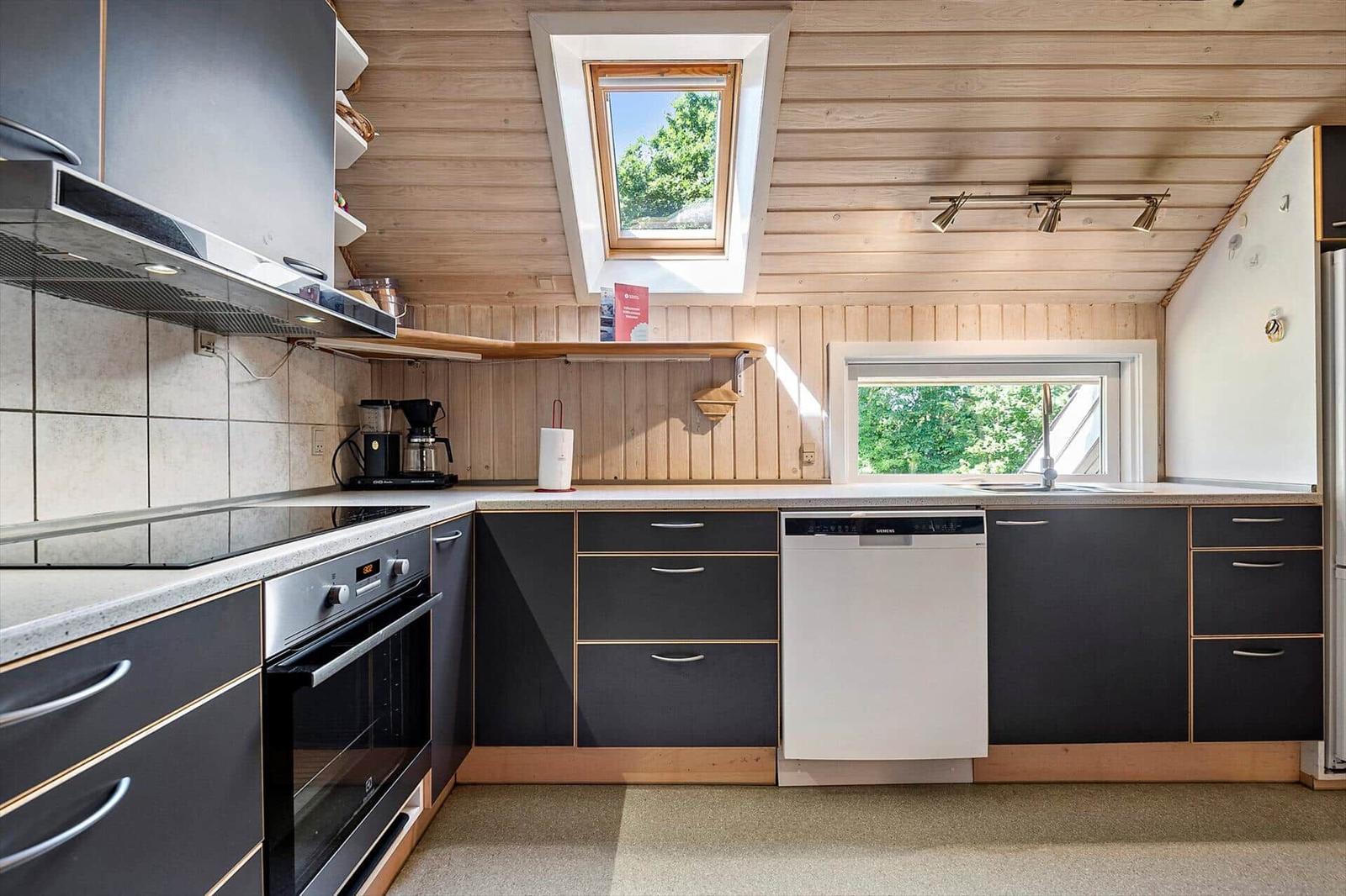 Küche mit schwarzen Schränken, Waschmaschine und Dachfenster. Holzwände und Arbeitsfläche.