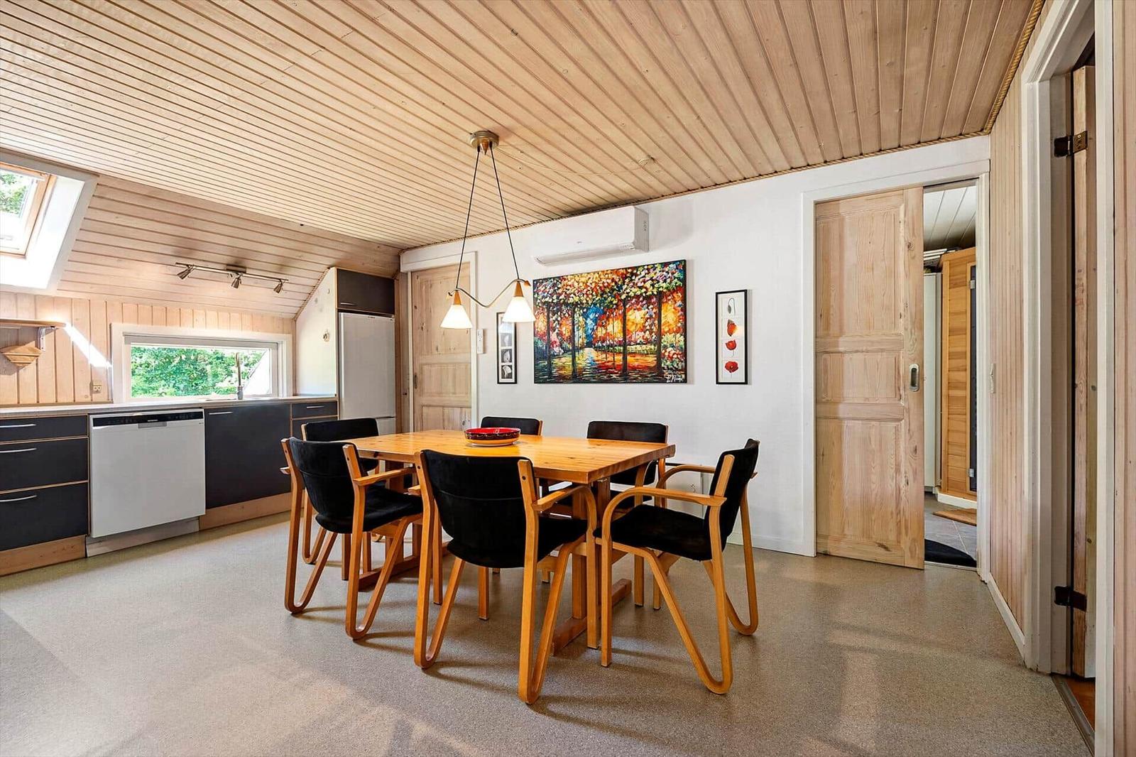 Essbereich mit Holztisch, schwarzen Stühlen und Küchenbereich im Hintergrund.