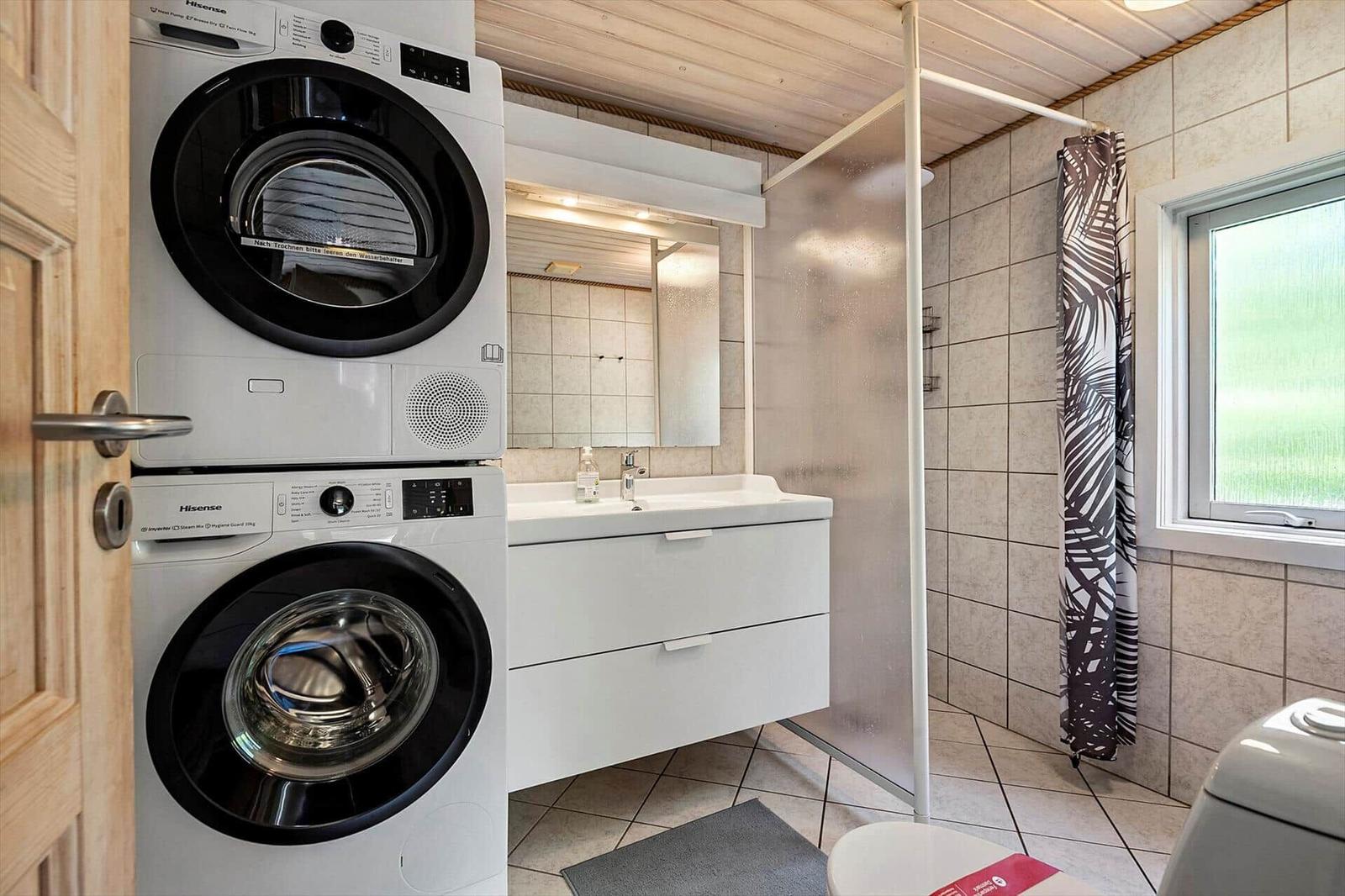Badezimmer mit Waschmaschine und Trockner, Waschtisch, Dusche und Fenster.